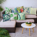 Funda de cojín hojas tropicales en sofá de terraza con mesa blanca y decoración natural