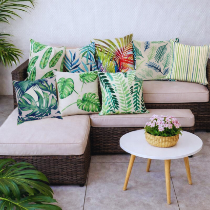 Funda de cojín hojas tropicales en sofá de terraza con mesa blanca y decoración natural